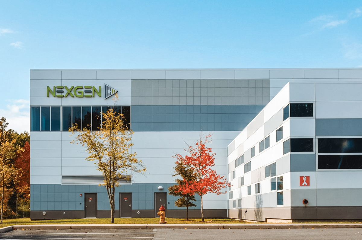 Exterior of a gray-and-white industrial building with a NexGen sign and autumn trees.